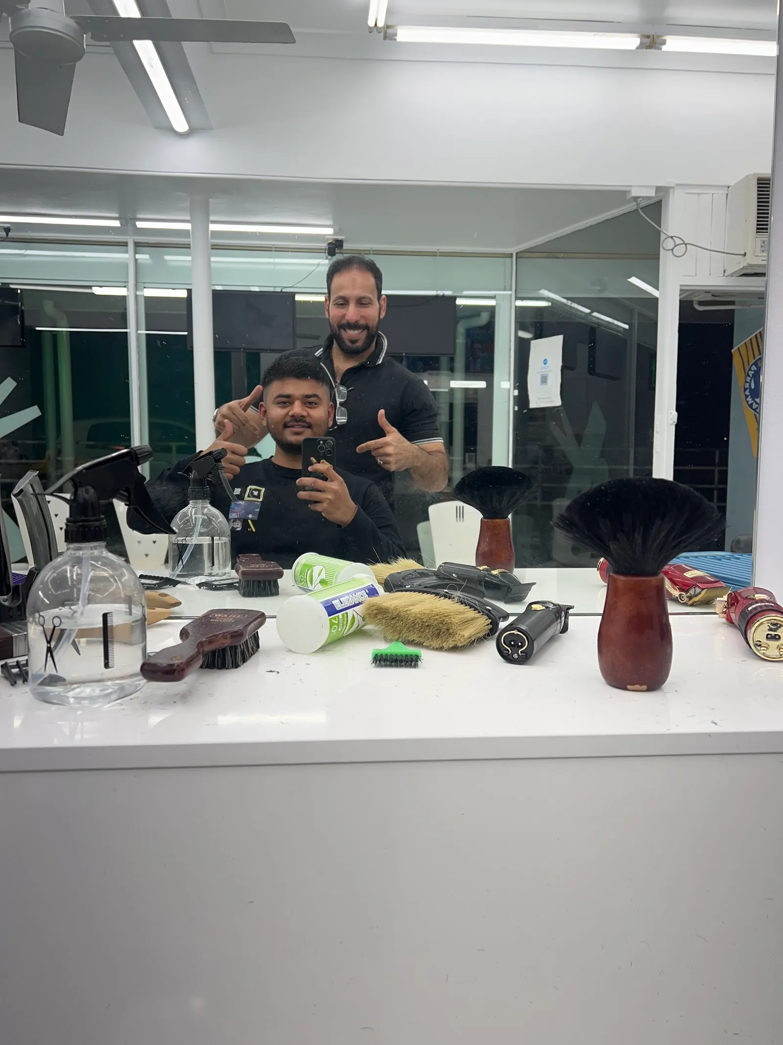 Two barbers smiling at the camera behind the counter